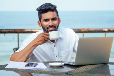 yakışıklı ve başarılı hintli adam şık iyi giyimli serbest çalışma dizüstü plajda.freelance ve uzak iş.işçi öğrenci hindistan okyanusu kıyısında çay bir yaz kafe fincan
