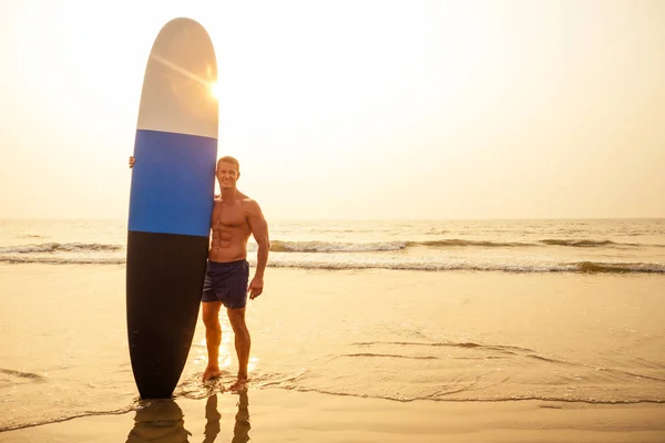 Surfen freelancing man staat met een branding in zijn handen op de kust. — Stockfoto