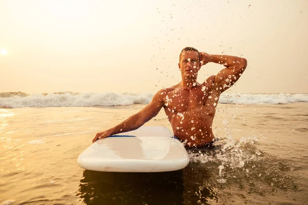 Surfen Freelancing man spier-en pers sport training op het strand bij zonsondergang. mannelijke fitness model surfer met een grote surfplank in de buurt van de Indische Oceaan Goa Ashwem Arambol Beach — Stockfoto