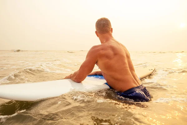 Surfer fitness man met een gespierd lichaam met zijn surfplank op het strand opwarmen. — Stockfoto