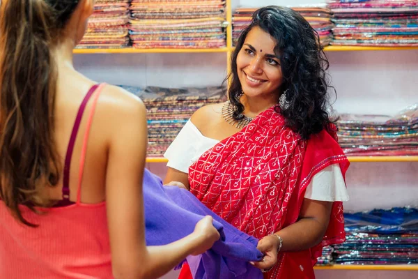 business lady in red traditional sari and jewelery clothes shop owner cashmere yak wool shawls and client.female seller in goa india arambol sale shop.designer seamstress tailor girl choosing fabric