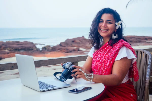 Mujer fotógrafa de la India fotografiando con cámara digital en la playa.hermosa mujer india en sari rojo tradicional en el paraíso tropical mar tomando fotos de la sesión de fotos del paisaje —  Fotos de Stock