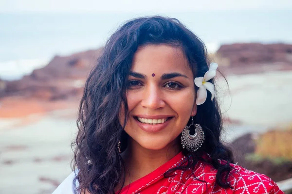 Indiano modelo de moda feminina de dentes brancos sorriso com flor em seu cabelo encaracolado na roupa tradicional da Índia sari casamento vermelho posando perto de árvores tropicais em uma praia paradisíaca mar ocean.wellness spa resort — Fotografia de Stock