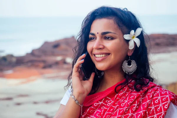 beautiful and young indian business woman in traditional india sari working with laptop by the sea.asian student girl remote work freelancer freelancing sitting on the beach using a smartphone phone