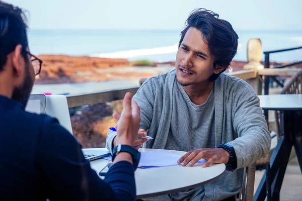 two happy businessmen discussing freelancer strategy in a meeting, Indian business man remote work freelancing sitting in a summer restaurant by the sea.successful deal on the beach tropical island