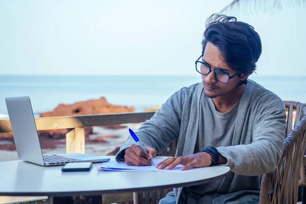 Schöner und erfolgreicher indischer Mann in einem stilvollen gut gekleideten Freiberufler, der mit einem Laptop am Strand arbeitet.Freiberufler und Fernarbeit.Geschäftsmann Student in einem Sommercafé am Ufer des indischen Ozeans — Stockfoto