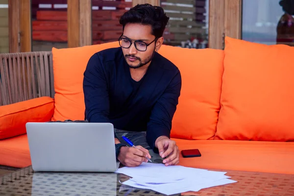 Freelancing and remote work.handsome male student working laptop keyboard sitting in cafe on the beach with free internet.Young indian man using computer in summer vacation by the sea — Stock Photo, Image