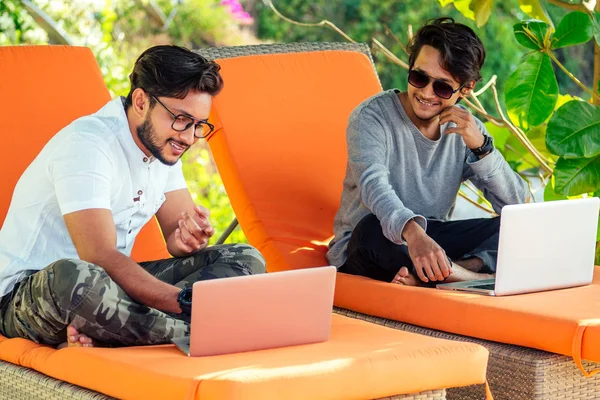 Indian young business people businessman freelancer working outdoors chaise lounge on the beach with laptop.two successful friends freelancing surfing remote work summer vacation in tropical paradise. — Stock Photo, Image