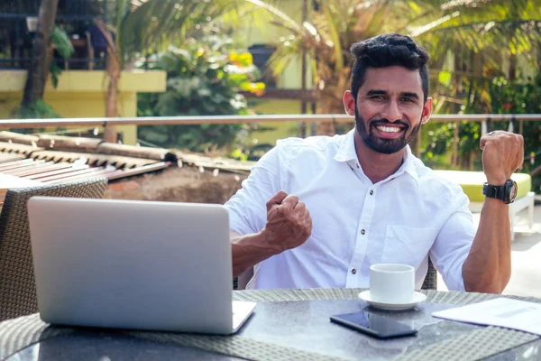 Handsome and successful indian man in a stylish well-dressed freelancer working with a laptop on the beach.freelance and remote work.businessman student in a summer cafe on the shore of india ocean — Stock Photo, Image