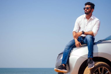 Başarılı genç işadamı güneş gözlüğü sahilde. Afro adam yolda yolculukta okyanus önünde park edilmiş arabasına yaslanmış barış ve sessizlik doğada rahatlatıcı zevk. Yaz tatilleri ve seyahat konsepti