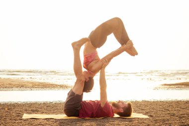 birlikte fitness yoga egzersiz yapıyor plajda iki genç adam ve güzel kadın. Deniz obuk goa hindistan günbatımında güç ve denge için Akroyoga elemanı