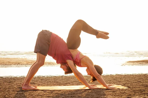 Два молодых человека и красивая женщина на пляже делают физические упражнения йоги вместе. Элемент Акройоги для силы и равновесия на закате Гоа Индиа — стоковое фото