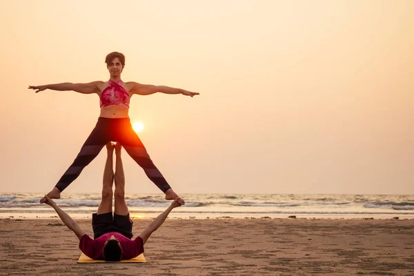 Δύο άνθρωποι που εξασκούνται στη γιόγκα στο ηλιοβασίλεμα στην παραλία της Ινδίας. θηλυκό και αρσενικό Acro γιόγκι Τάντρα που πετάει αντίγραφο — Φωτογραφία Αρχείου