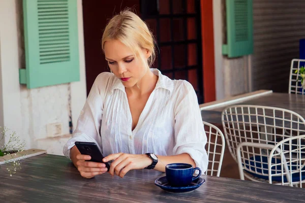 Bir kafede akıllı telefon kısa mesaj yazarak kadın. Cep telefonu kullaranarak bir kahve ile bir masada oturan genç kadın.