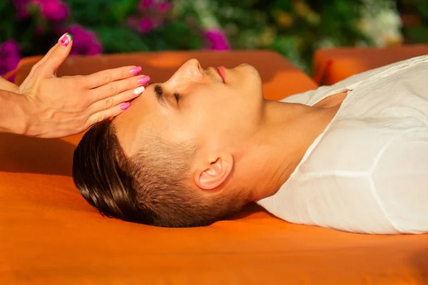 Mann med olje-Ayurveda spa-behandling, stilig skjegg, mørkhåret, mannlig modell som slapper av på stranden, spa og avslapningskonseptet plumeria og kokosnøtt – stockfoto