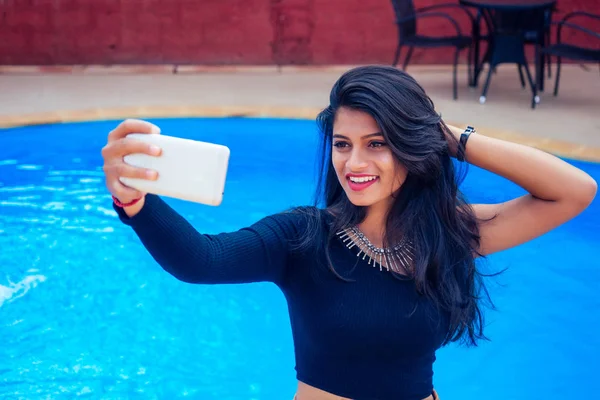 Hermosa mujer india toothy sonrisa blanca selfie retrato en la cámara del teléfono inteligente café de verano por el mar junto a la piscina goa —  Fotos de Stock