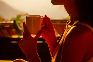 Beautiful woman with cup of coffee tea enjoying the view from the balcony on tea plantation jungle at India Kerala Goa wildernest nature spa resort