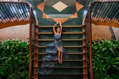 Uzun tren ile gri mavi elbise güzel gelin kadın klasik bir iç merdivenlerden tırmanıyor. tropikal cennette lüks ve zengin lüks otel