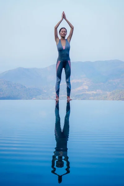 Beautiful woman practice yoga pose on the infinity pool above the mountain peak in the morning in front of beautiful nature views in india goa wildernest nature resorte .romance sunrise in mountains