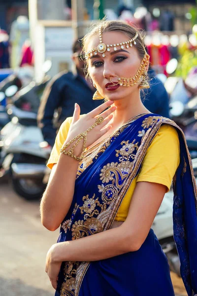 Indisk vacker kaukasisk kvinna i traditionell blå klänning. hinduisk modell med gyllene kundan smycken set Bindi och näsa ring piercing Nath modefotografering på gatan bland motorcyklar och marknaden — Stockfoto