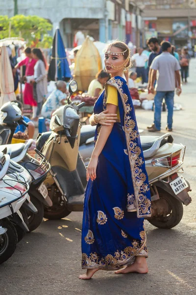 Indisk vacker kaukasisk kvinna i traditionell blå klänning. hinduisk modell med gyllene kundan smycken set Bindi och näsa ring piercing Nath modefotografering på gatan bland motorcyklar och marknaden — Stockfoto