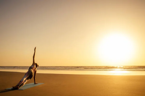 Силуэт молодой женщины в стильном костюме для йоги-комбинезона, занимающейся йогой на пляже в позе копировального пространства — стоковое фото