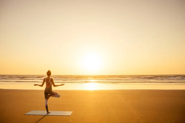 Силуэт молодой женщины в стильном костюме для йоги-комбинезона, занимающейся йогой на пляже в позе копировального пространства — стоковое фото