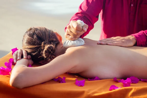 Mulher de massagem relaxante ayurvédica no salão de spa recebendo massagem na praia de férias.Menina bonita desfrutando resort spa dia, deitado na composição de spa procedimento de tratamento de mesa com sacos de ervas — Fotografia de Stock