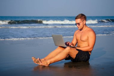 yakışıklı ve başarılı bir adam şık iyi giyimli freelancer çalışan dizüstü plajda lotus pozisyonda meditasyon.freelance ve uzak iş.işadamı namaste ve om okyanus