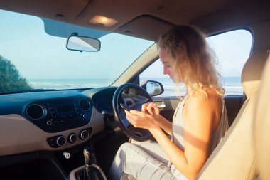 Young woman sitting in car and talking on the phone sunset on the waterfront.navigator map