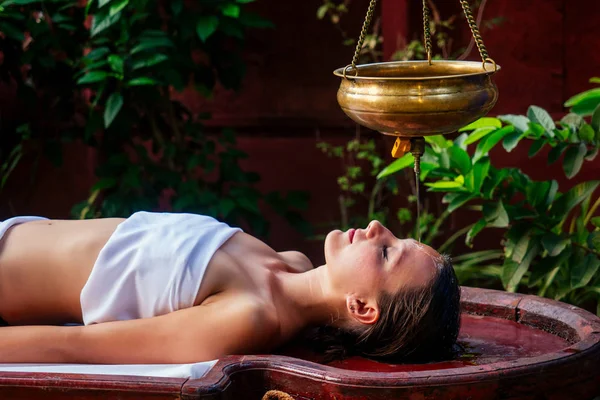 Ayurveda massage alternative healing therapy.beautiful caucasian female getting shirodhara treatment lying on a wooden table in India salon — Stock Photo, Image