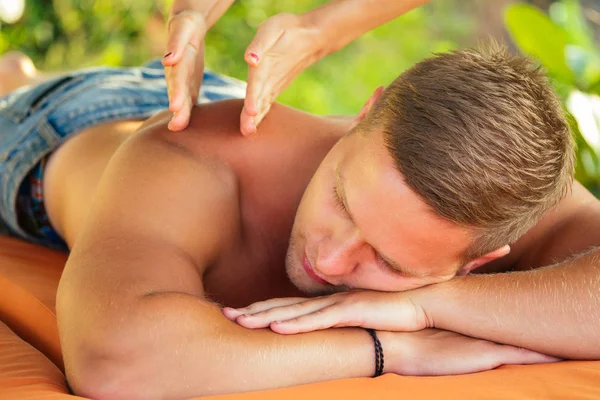 man having oil Ayurveda spa treatment.handsome bearded dark haired male model relaxing on beach.spa and relaxation concept plumeria and coconut