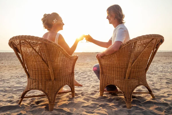 Силует пара в любові сидить на плетених стільців і заклеплячих келихів з напоями на пляжі з видом на захід сонця день Святого Валентина — стокове фото