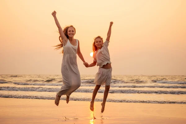 Щаслива мати і молода дочка на пляжі на заході сонця розважаються на узбережжі. граючи стрибки і радісна жінка і її дитина копіюють простір копіювання копій — стокове фото
