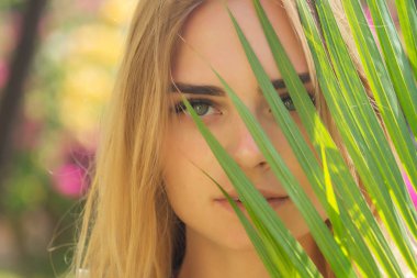 close up portrait face blond woman thick eyebrows like Cara Delevingne with palm branch