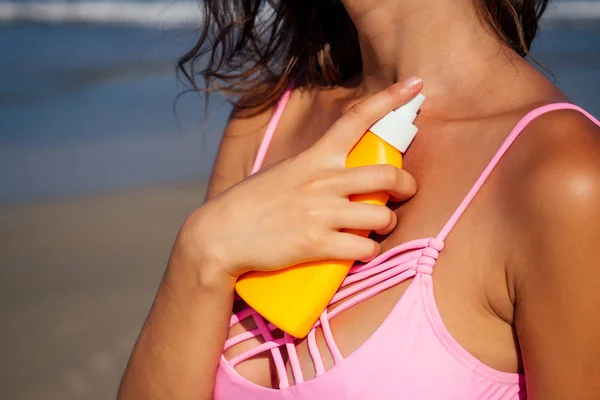 Hermosa mujer bronceada fitness tetas grandes modelo celebración de botella spf aplicar en el pecho en un traje de baño elegante de moda en el mar océano playa cielo azul y palmeras background.summer vacaciones — Foto de Stock