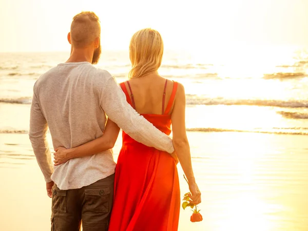 Two lovers people at sunset by the sea romance and tenderness feelings first love date.man and woman blonde in a dress on the beach with a rose sun rays.Valentines day and International Womens Day — Φωτογραφία Αρχείου