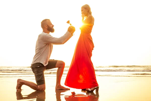 浪漫2月14日情人节暑假，恋爱约会。爱夫妇与花束男子在白色衬衫和金发女子在长裙与玫瑰在他的手在海滩上 — 图库照片
