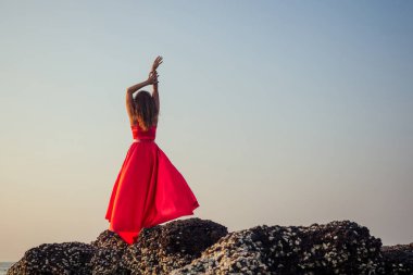 Güzel kadın mavi gökyüzü ve Goa denizi üzerinde bir uçurumun üzerinde duruyor. Kırmızı ipek elbise copyspace esmer kız