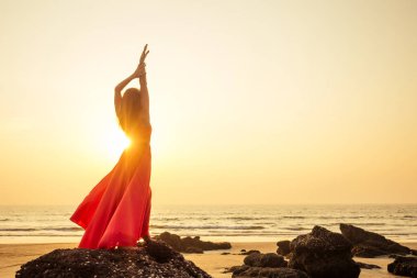 Güzel kadın mavi gökyüzü ve Goa denizi üzerinde bir uçurumun üzerinde duruyor. Kırmızı ipek elbise copyspace esmer kız