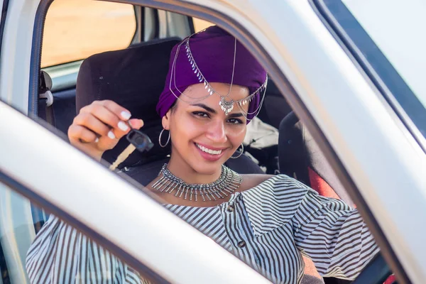 cheerful young african american woman in a purple turban on head showing her new car key at summer beach.indian female person enjoying a new car purchase