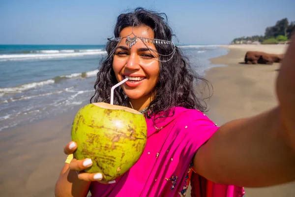 Красивая индийская женщина делает фото селфи на камеру телефона в розовом стильном сари, зубастая белая улыбка солнца летом на море Гоа. концепция здорового питания — стоковое фото