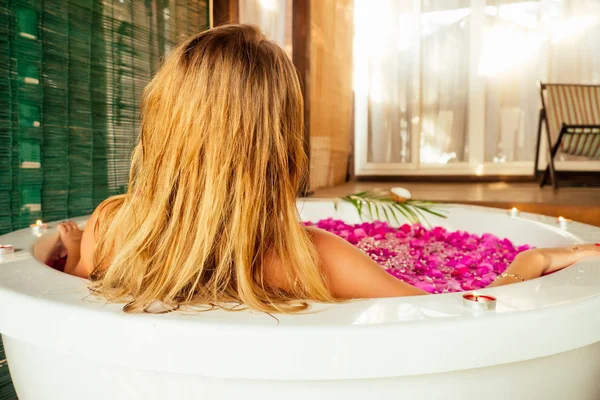 Attraktive nackte Frau genießt ein Bad mit Milch und rosa gelben tropischen Blumen und Kerzen — Stockfoto