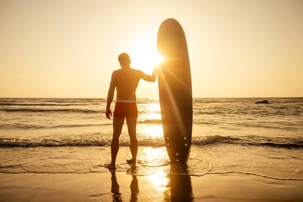 Surfer met surfplank kijkend naar zonsondergang bij Goa India — Stockfoto