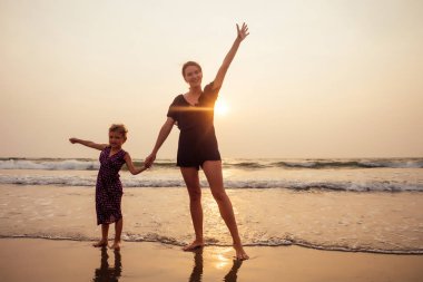 anneler Günü kavramı sevgi, ebeveynlik ve mutlu bir aile. Anne ve çocuk kızı sahilde gün batımında eğleniyor