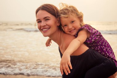anneler Günü kavramı sevgi, ebeveynlik ve mutlu bir aile. Anne ve çocuk kızı sahilde gün batımında eğleniyor
