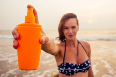 Plajda güneş kremi şişesi tutan güneş kremi ile güzel bir gülümseyen kadın portresi