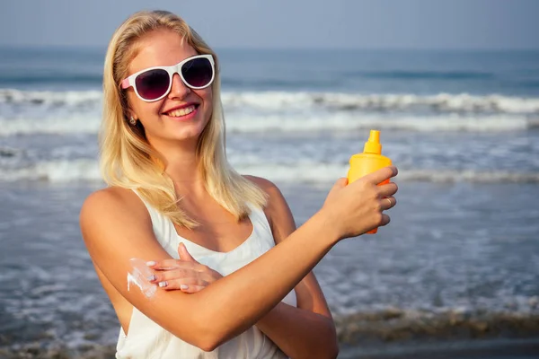 Tan woman applying sun protection lotion in white dress and glasses on the beach — Stock Photo, Image