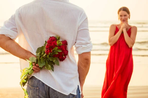 海のビーチで彼の驚きと不思議な女性にバラを与える男。ロマンチックなデートや結婚式やバレンタインデーのコンセプトは海で.愛するカップルは3月8日の女性の日と幸せな誕生日を祝う — ストック写真