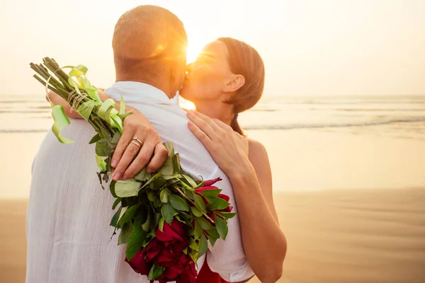 Esposa e marido casal feliz em férias pelo sea.beautiful mulher em vestido vermelho com um anel no dedo e homem amoroso em uma camisa branca com um buquê de rosas românticas sunset.Valentines dia data — Fotografia de Stock